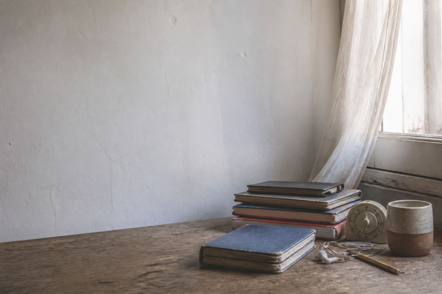 A collection of well-used Spanish study notebooks beside a timer in soft morning light