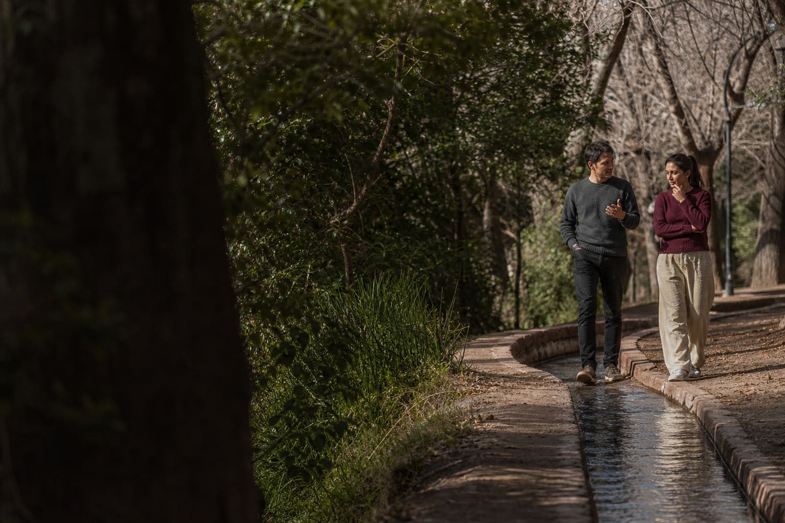 Coach y estudiante conversan mientras caminan junto a una acequia arbolada de Mendoza
