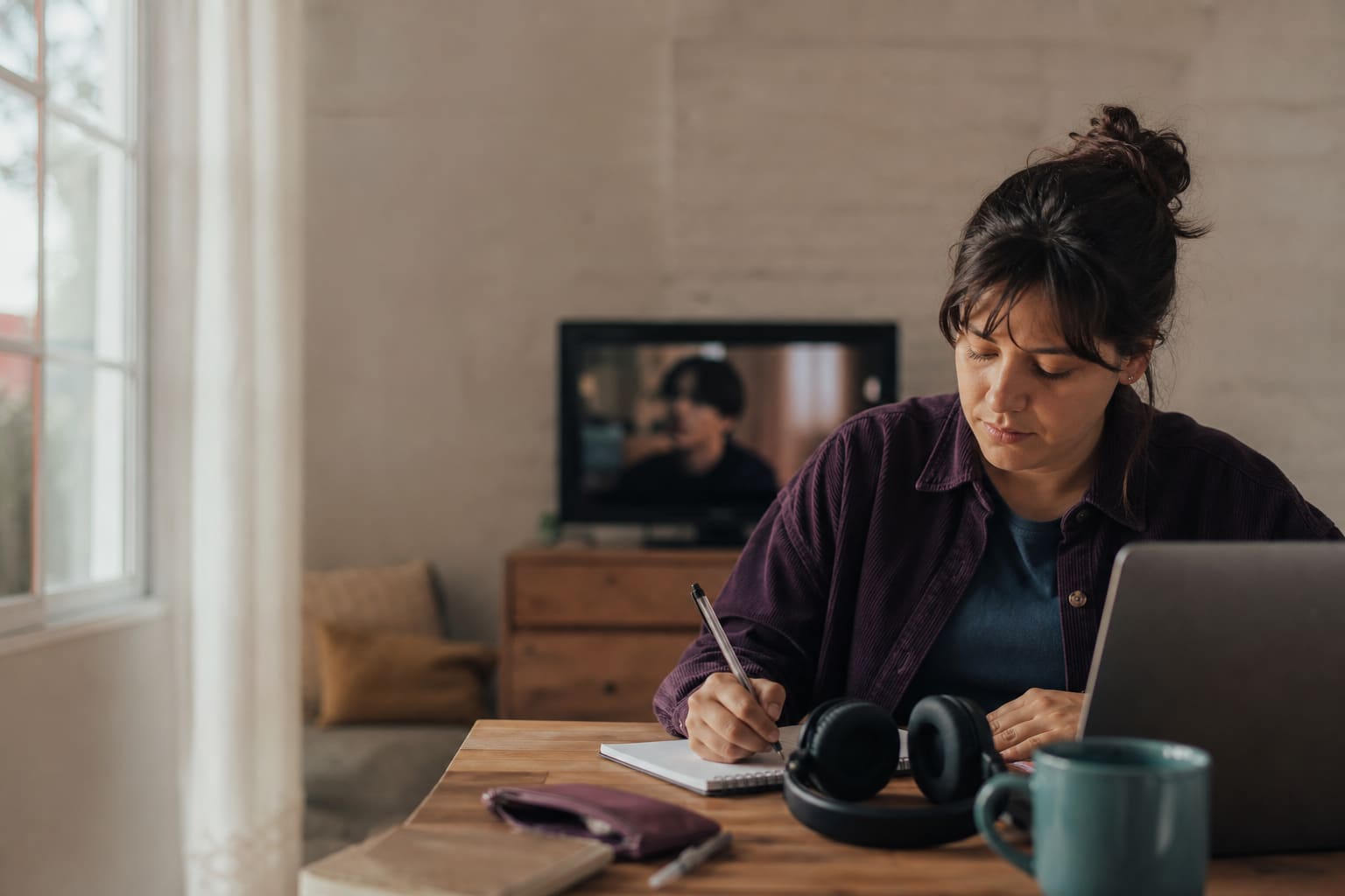 Estudiante adulta practicando inglés con una serie y tomando notas en casa